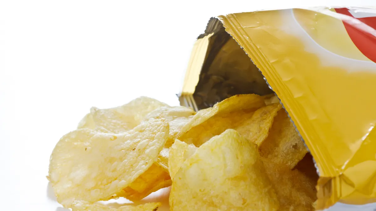 Side view of a bag of open potato chips, with chips spilling out