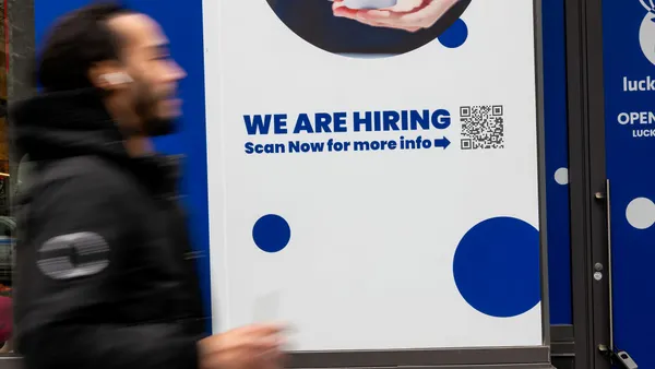 A person walks by a "now hiring" sign bearing a QR code.