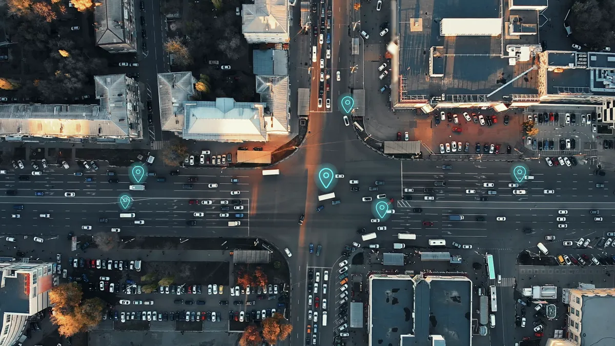 A creative image of an aerial view of a city intersection with many cars and GPS navigation system symbols. Autonomous driverless vehicles in city traffic.