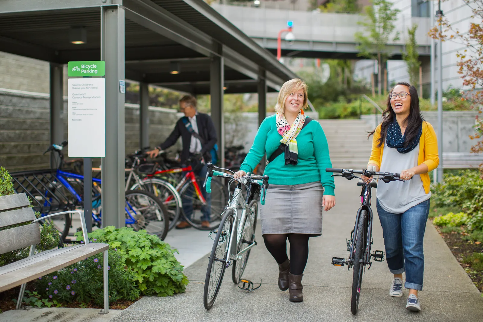 Two people walk with their bikes in an industrial complex.