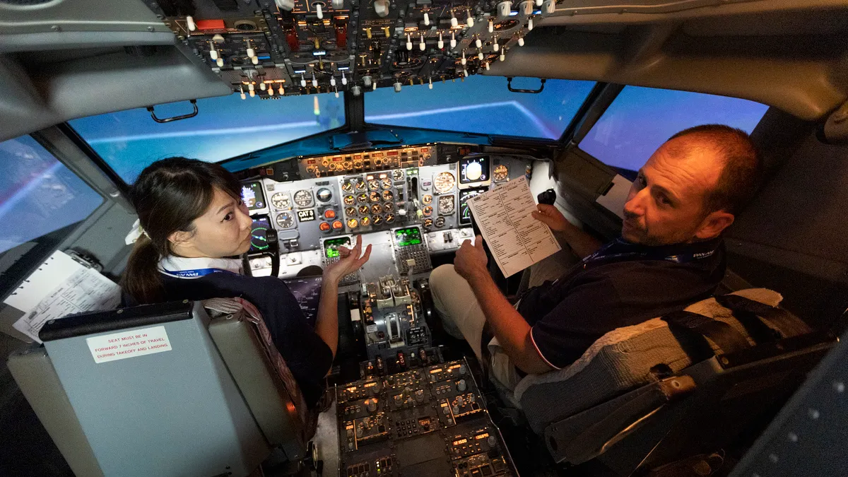 Two people sit in a flight simulator cockpit.