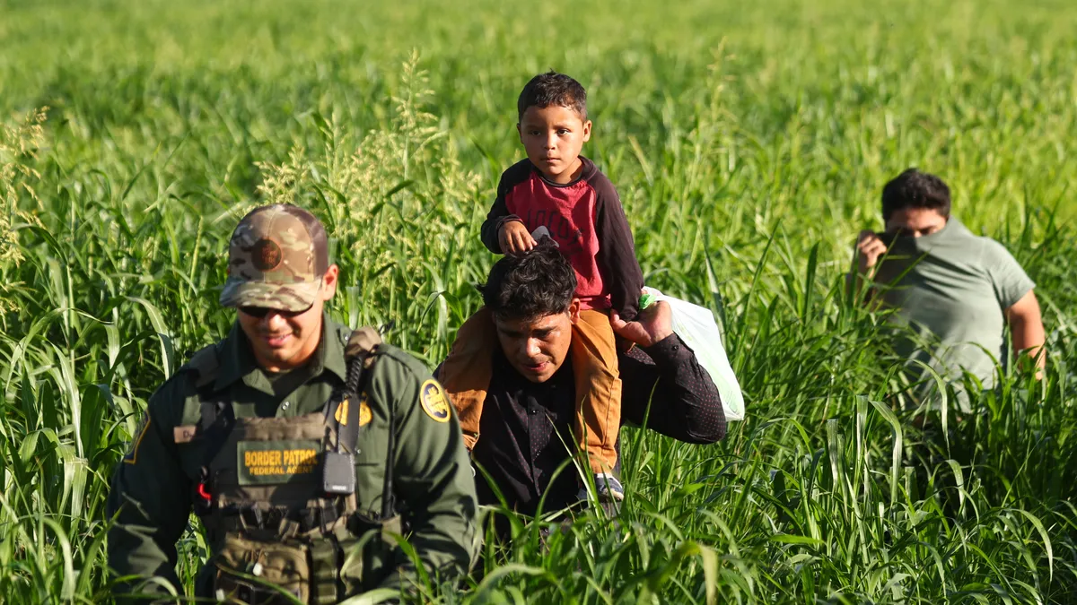 A man in uniform leads another man and a child through a farmfield.