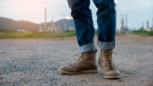 A low angle of a workers' legs in denim and boots standing in gravel.