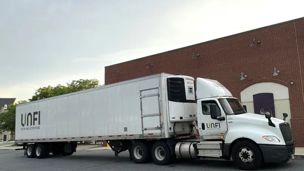 A white tractor-trailer in front of a red brick building.