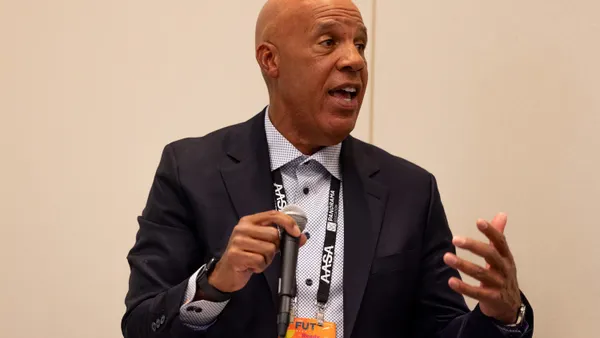 Adam Clark speaks into a microphone with his hand gesturing toward the audience