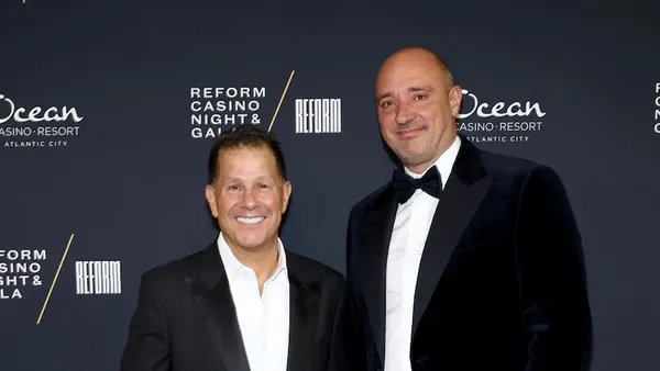Two people in dark suits and white shirts, the one on the right wearing a bow tie.