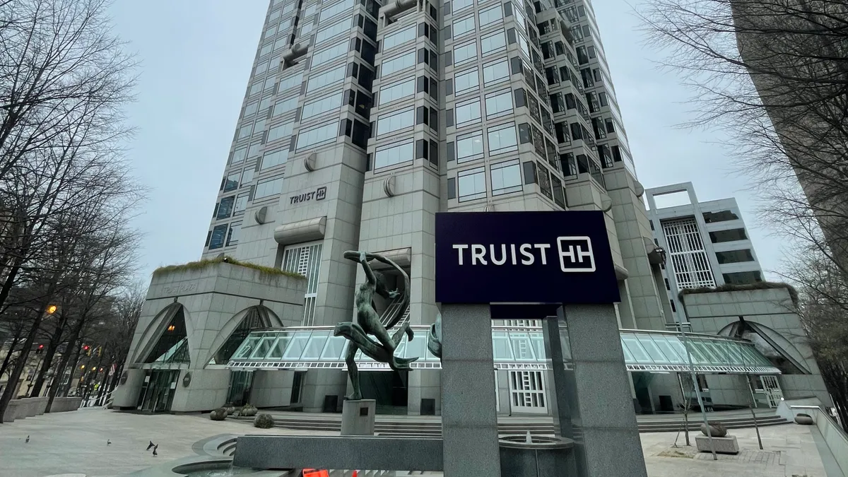 Truist plaza is shown, with a sign reading "Truist" and the company's logo in the foreground, and the skyscraper in the background.