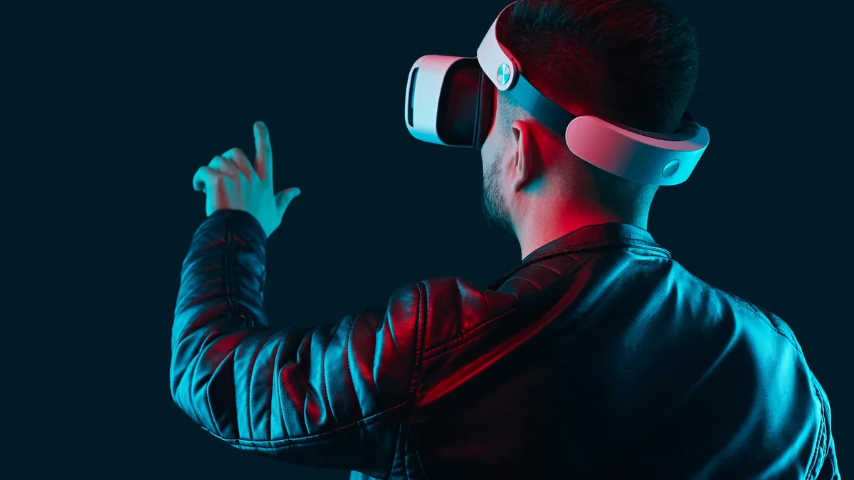 Back view of male player touching invisible screen while experiencing cyberspace, in VR glasses on dark background in studio with pink and blue neon lights