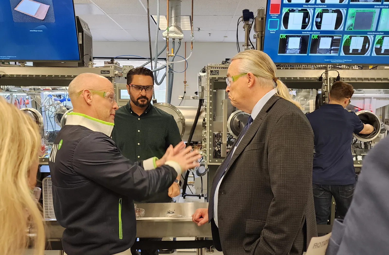 Three men wearing protective glasses in front of machinery.