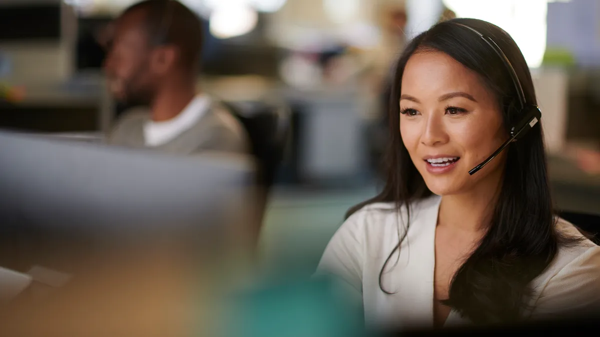 A woman talks on a headset in front of a computer.