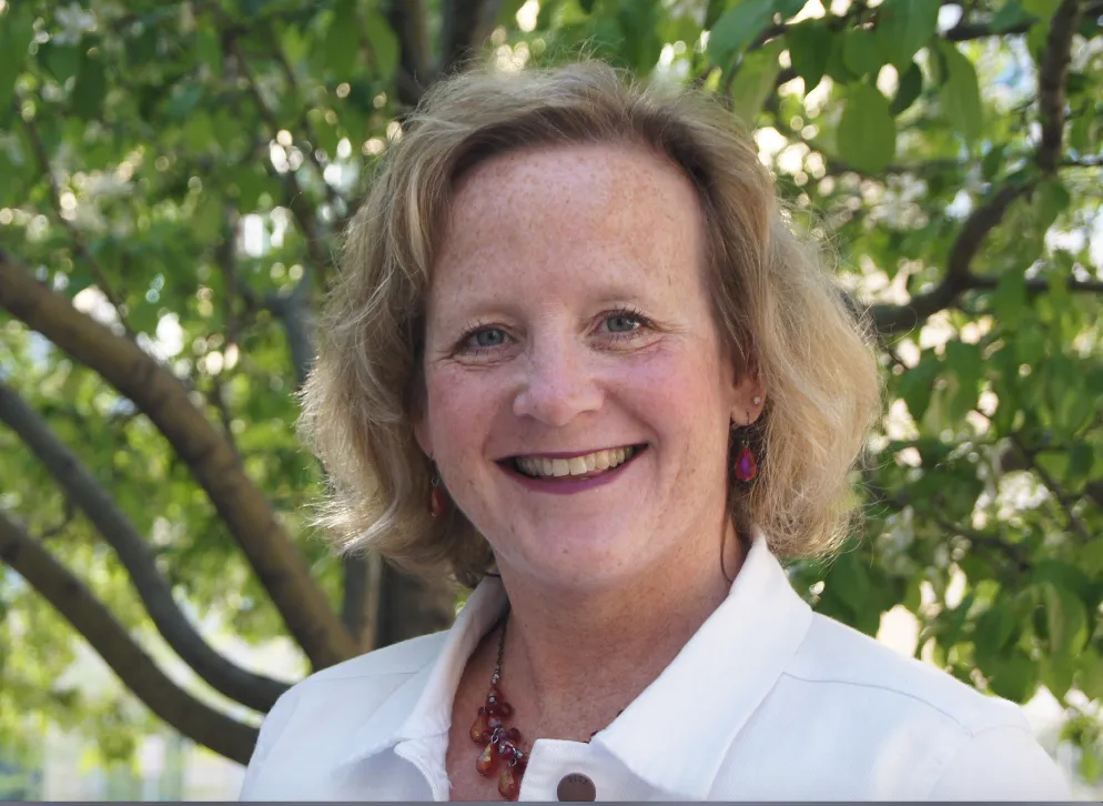 Profile photo of adult in white shirt with green trees in the background