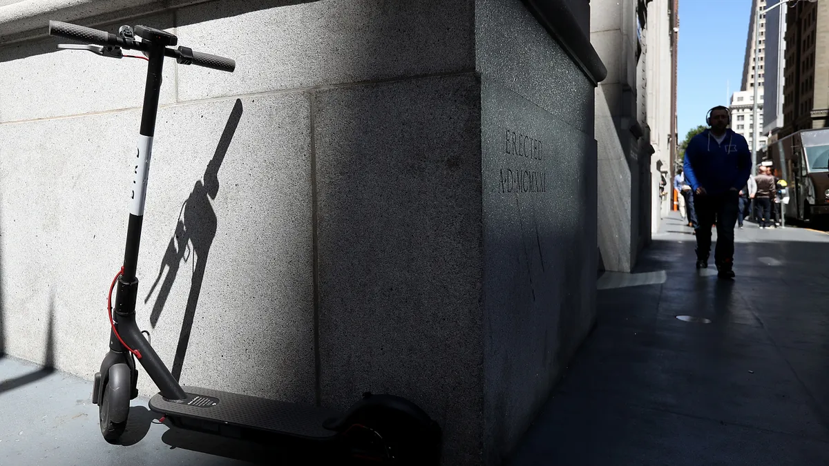 An e-scooter on a sidewalk next to a building casts a shadow on the building