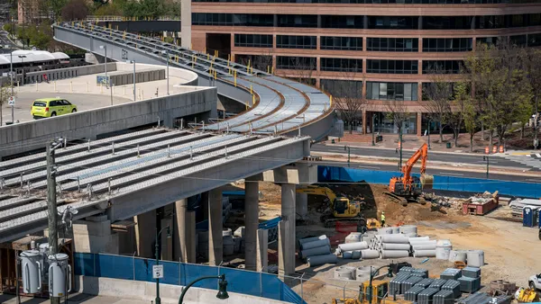 View of a jobsite with construction equipment and debris, under an elevated rail platform.