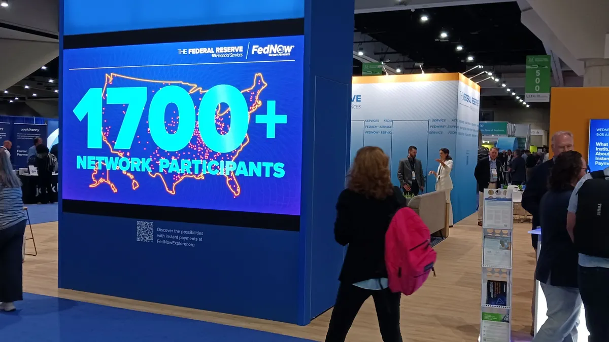A digital sing at a conference shows the number 1700 under a FedNow logo, with attendees milling around.