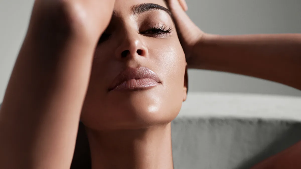 Kim Kardashian's face is shown in a close-up with one hand to the side of her head.