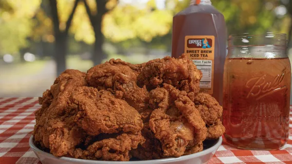 A photo of a place of fried chicken on a table outdoors with a red checkered tablecloth under it and a glass and jug of tea behind it.