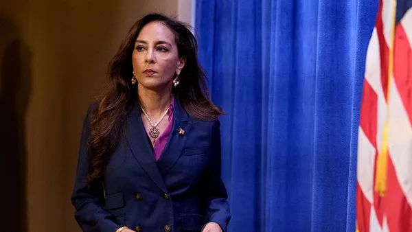 Harmeet Dhillon walks with papers in hand on a stage.