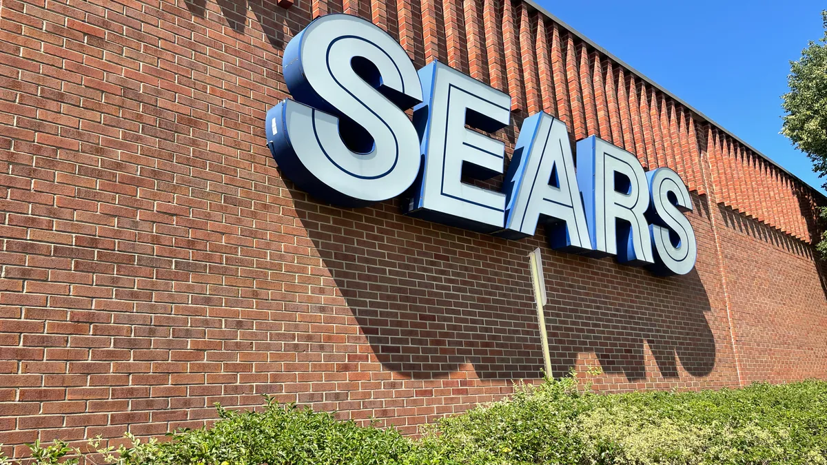 Sunlit Sears sign over a hedge.