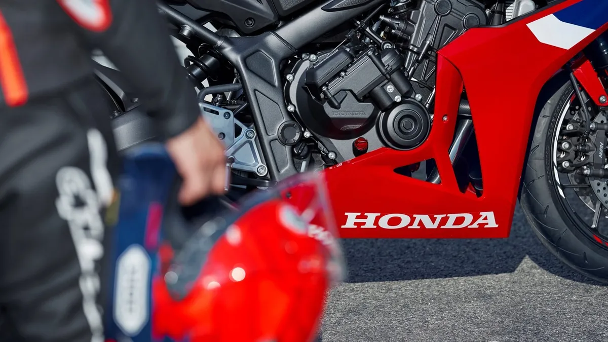 A person carrying a helmet walks toward a motorcycle. The motorcycle has the word "Honda" on it.