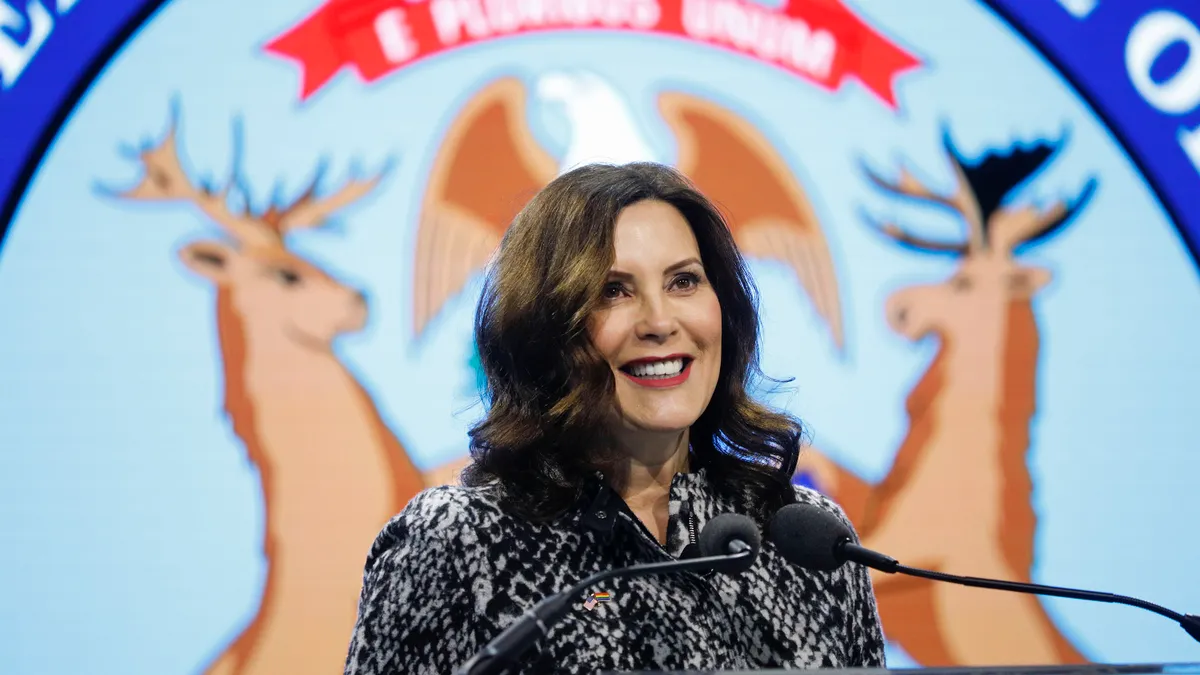 A politician stands in front of a podium with the seal of Michigan projected behind her.