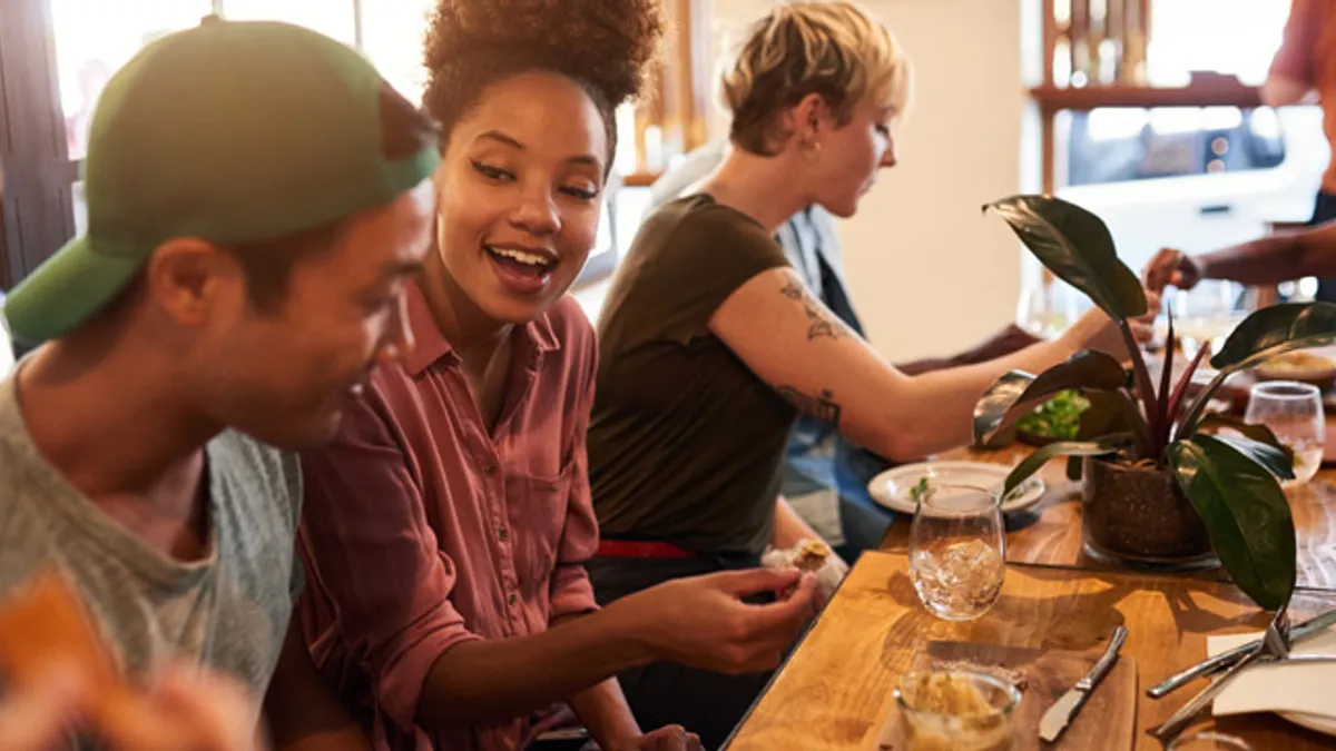 Group of smiling young friends talking together over lunch and drinks at a table in a trendy bistro.