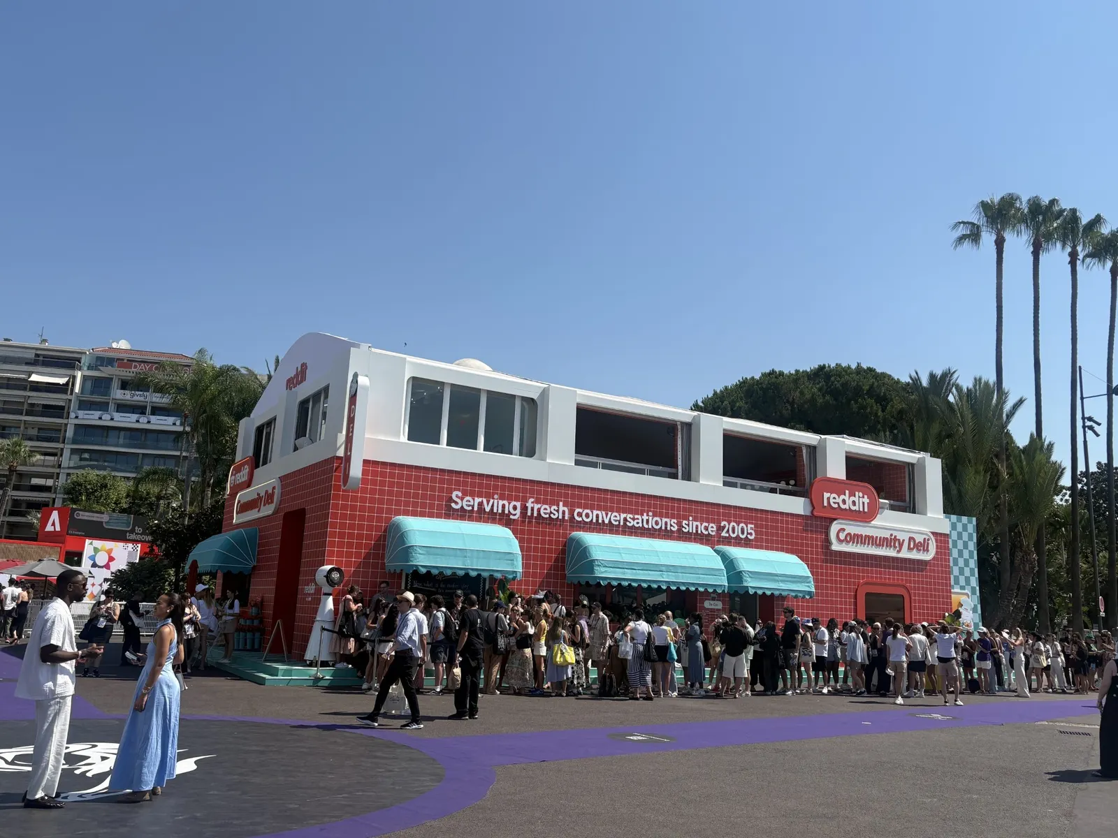 Cannes Lions attendees line up outside of a deli-themed Reddit activation on the festival promenade.