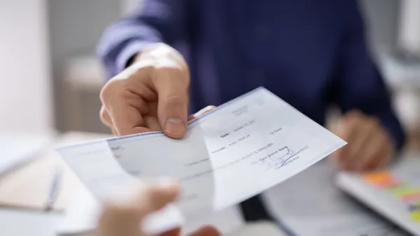 A businessperson hands a colleague a paycheck.