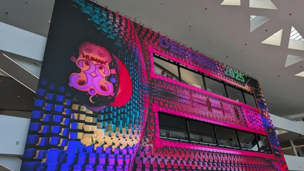 A massive electronic screen that says "DEF CON 2025" and "HUMAN 33" hangs in a large atrium.