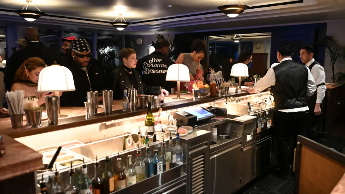Guests gather around a bar as bartenders mix drinks.