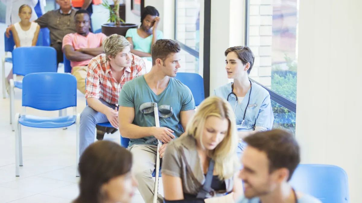 A provider and a patient talking while surrounded by other patients in a hospital waiting room.