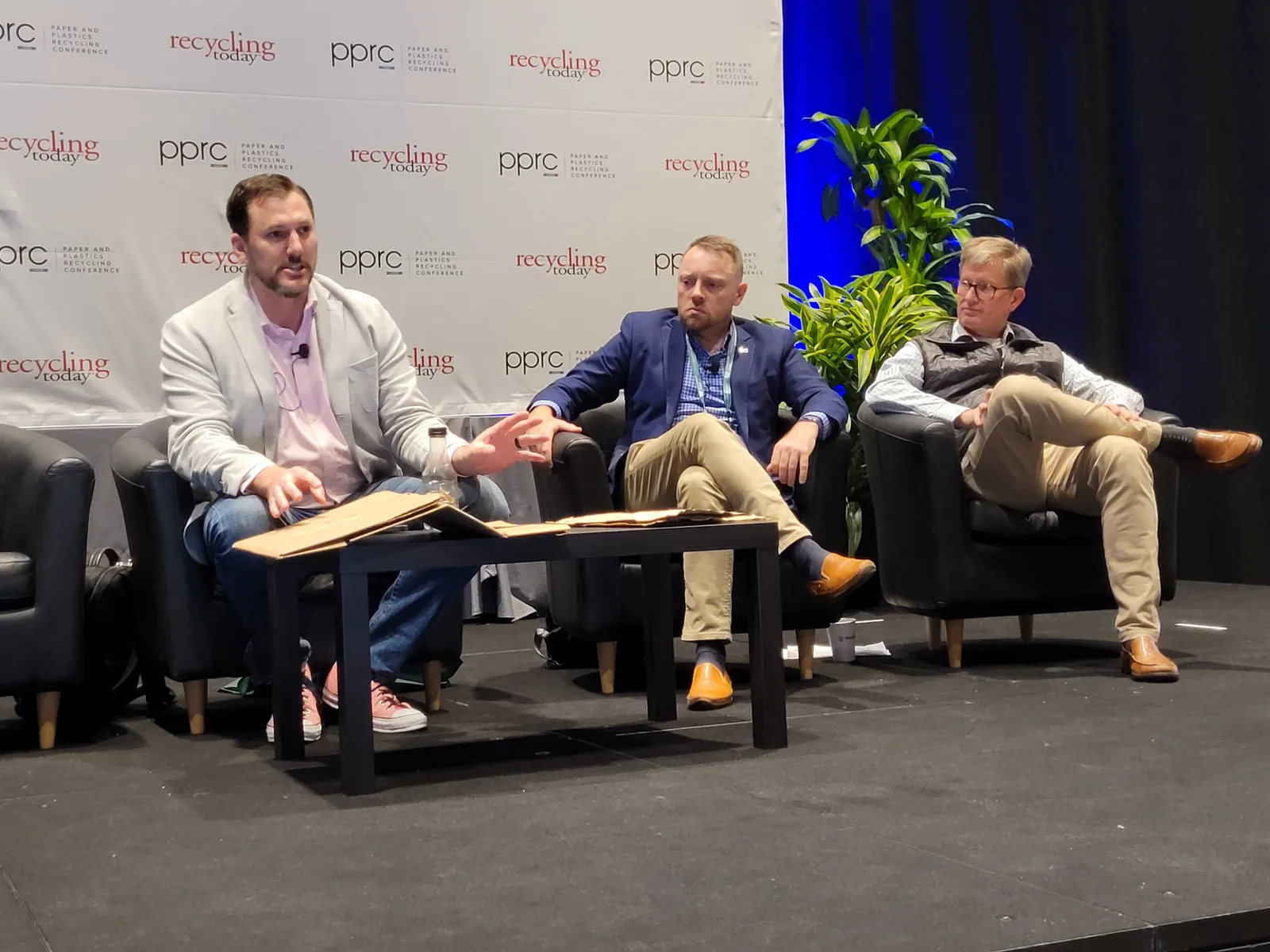 Three people sitting on chairs on a stage at a conference.