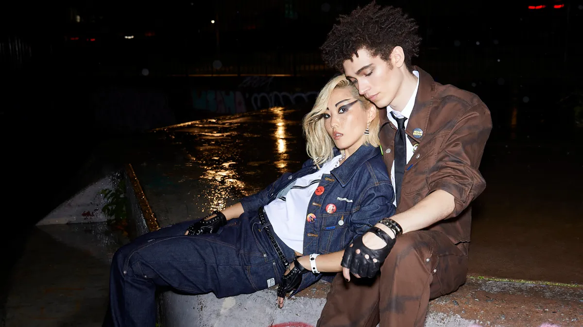 Two people wearing clothes from the Lee and Roaringwild collection lean into each other seated on concrete.