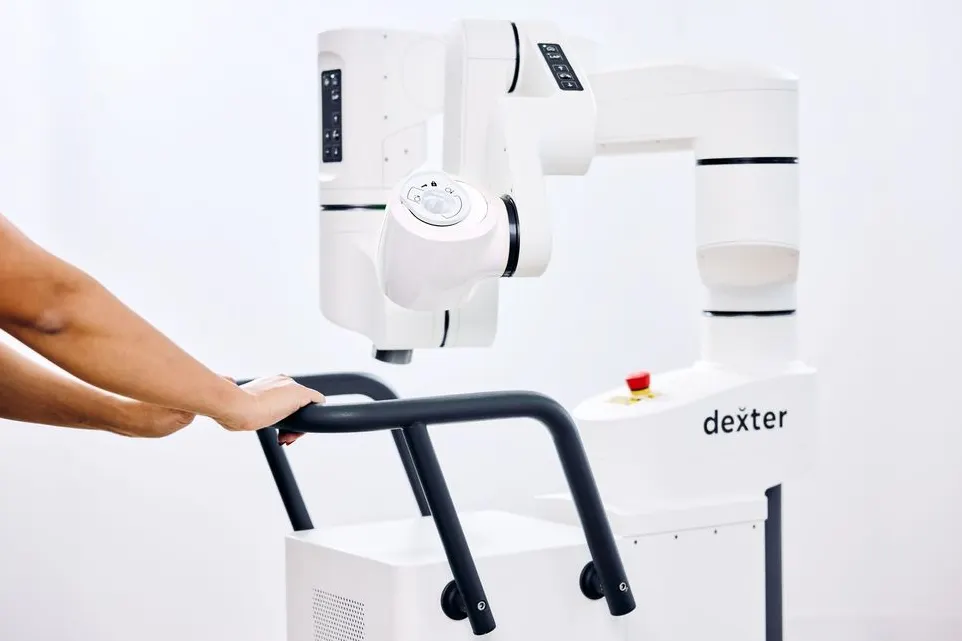 Two hands grasp a handle used to push a robotic surgery cart.