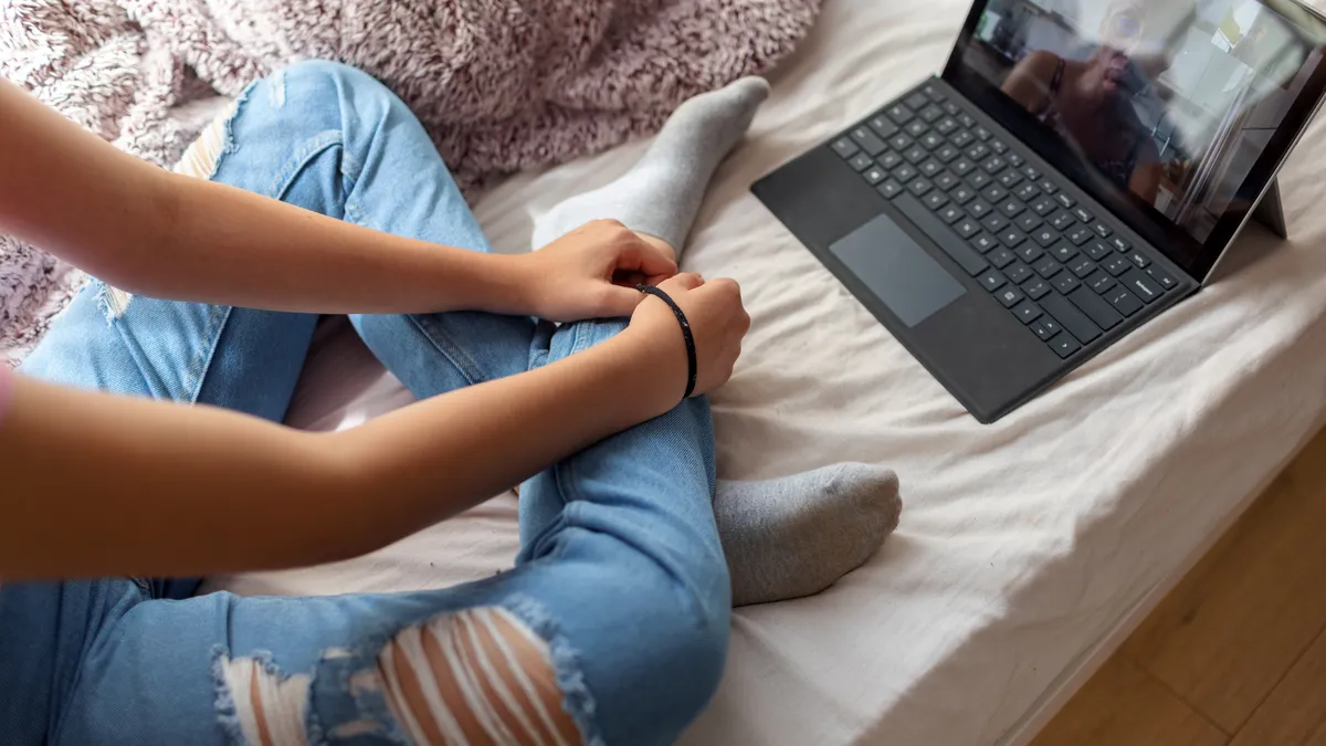 A cropped picture of a person sitting on their computer with a laptop.