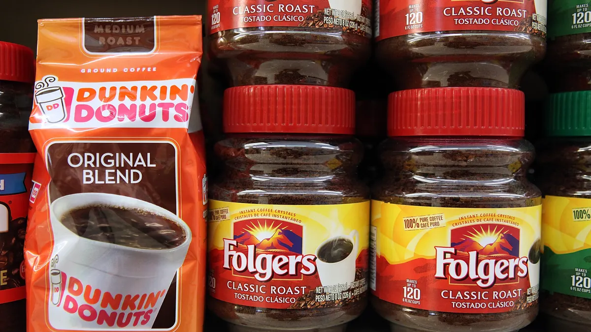 A bag of Dunkin' coffee sits on a store shelf next to stacks of Folgers instant coffee jars