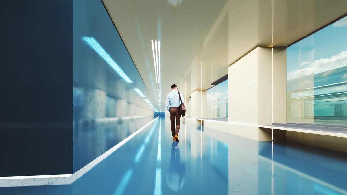 A rear view of a man walking down a modern business office corridor