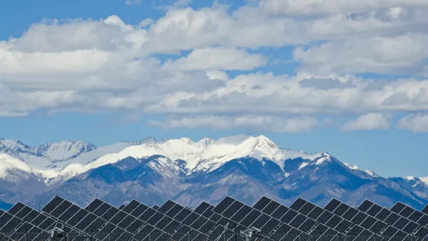 A row of solar panels with snow capped mountains in the background.