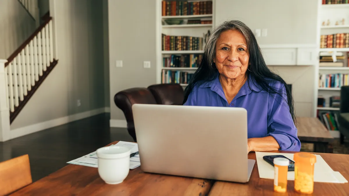 An Indigenous person sits at their kitchen table, looking at their laptop