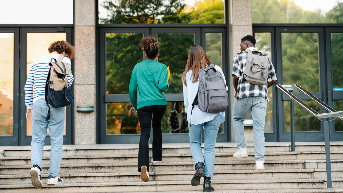 Four college students walk up the steps to a building entrance.