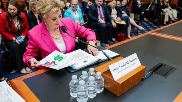 Linda McMahon sorts through her documents at a desk while people are seated behind her.