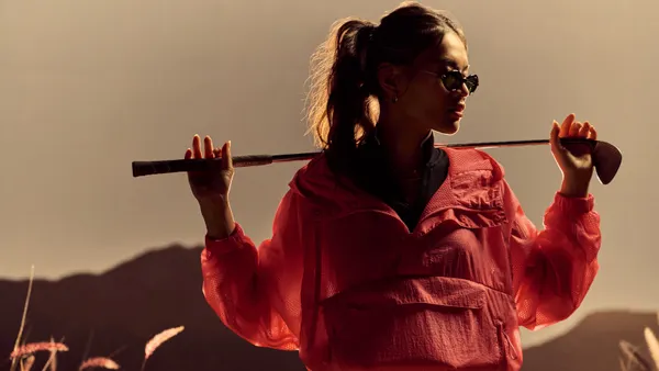 A person in a pink windbreaker holds a golf club behind their head.