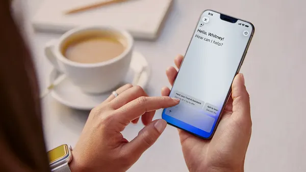 A person using the Ford vehicle app on a smartphone with a cup of coffee shown on a table.