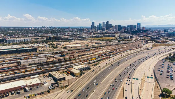 A high angle view of cars driving along a highway with the Denver metro area building skyline in the background.