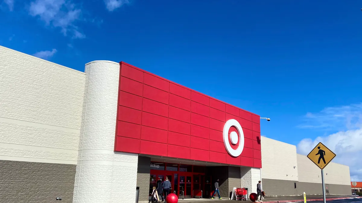 A big box store with a red storefront decorated with a white target sits against a bright blue sky. A walk sign is on the lower right.