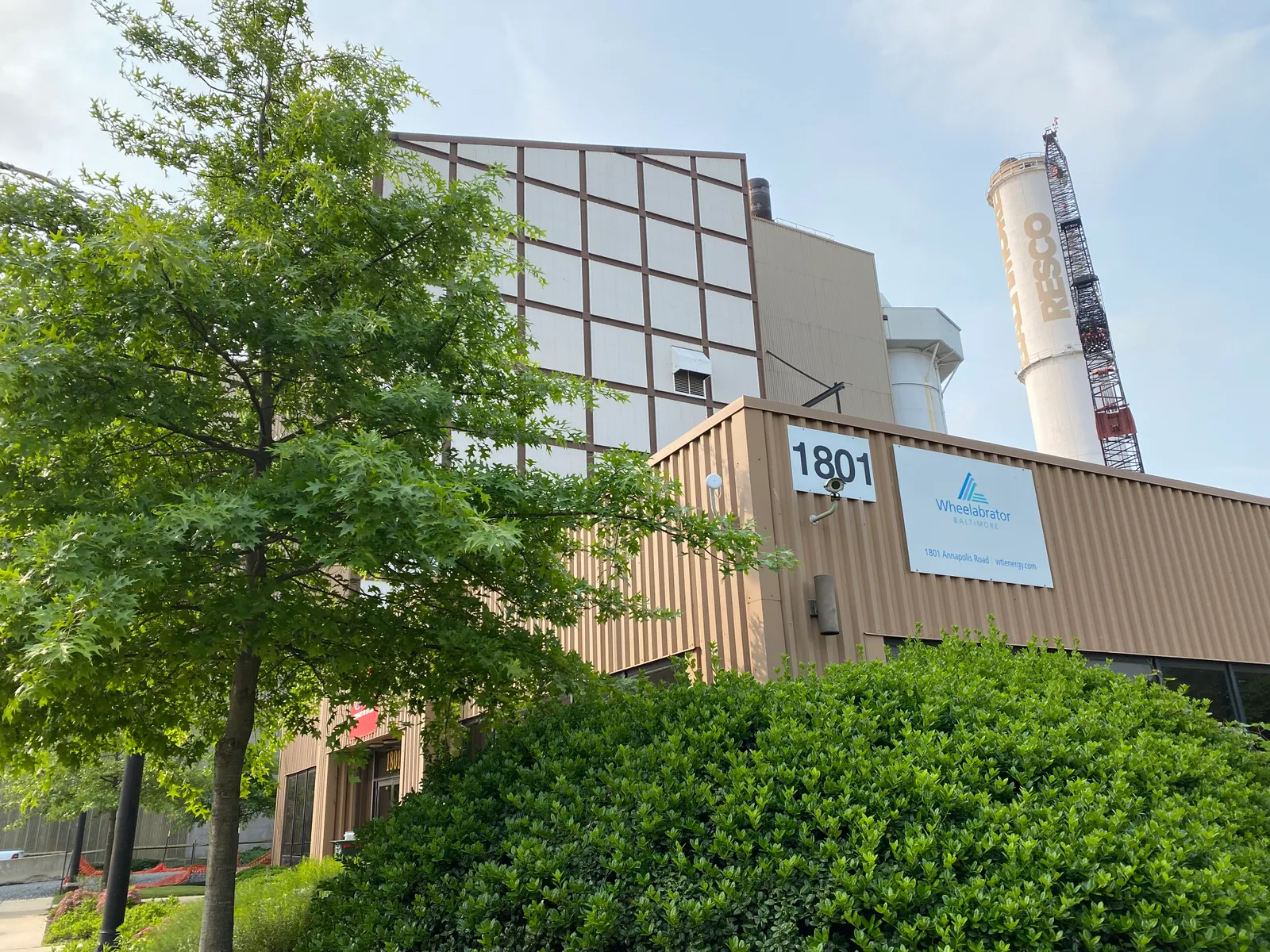 An industrial facility with boilers rising behind a nondescript building with a sign reading "Wheelabrator Baltimore."