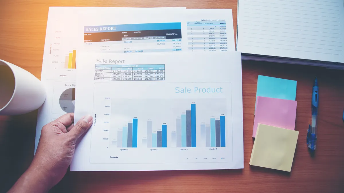 A person's hand is pictured holding a piece of paper containing several bar charts illustrating sales increases.