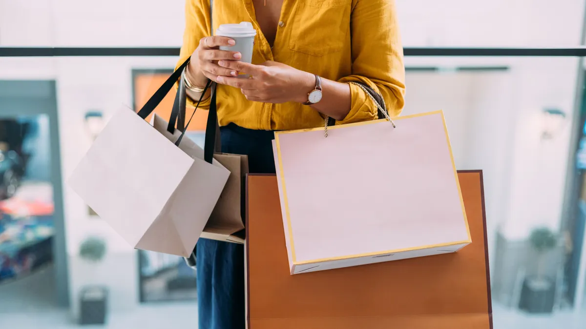 A person holds multiple shopping bags and a coffee cup.