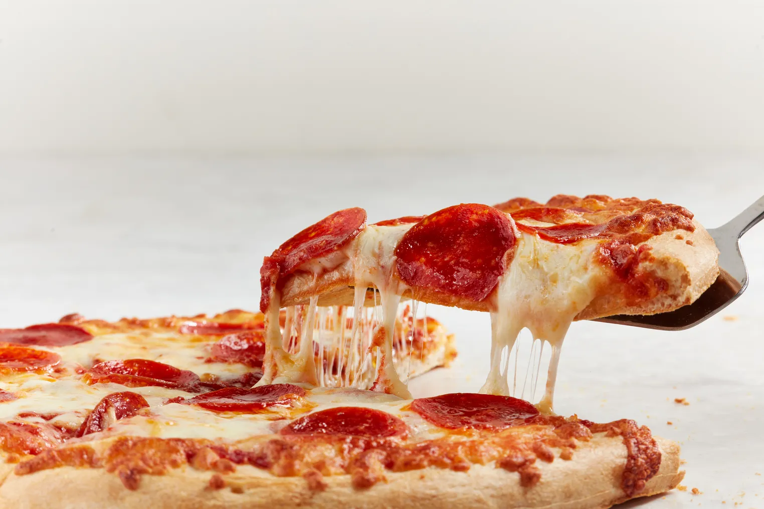 A photo of a pizza on a white background, with one slice being pulled up and away.