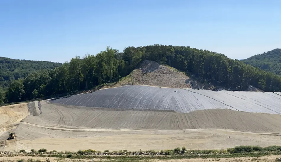 A large mound devoid of vegetation with a small dumpster in the corner