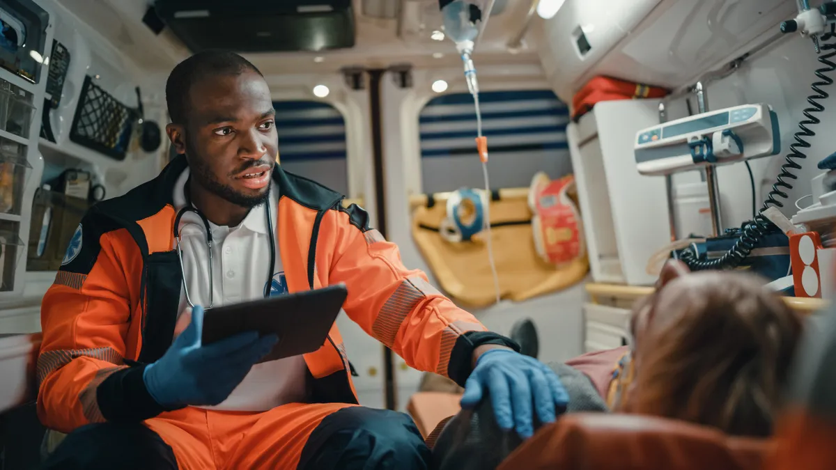 EMS Professional Paramedic Using Tablet Computer to Fill a Questionnaire for the Injured Patient on the Way to Hospital.